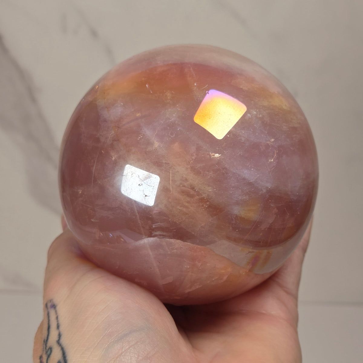  iridescent crystal sphere in pink, peach, and reddish tones displayed on clear stands atop gold-colored hexagonal pedestals against a light marble-patterned background.