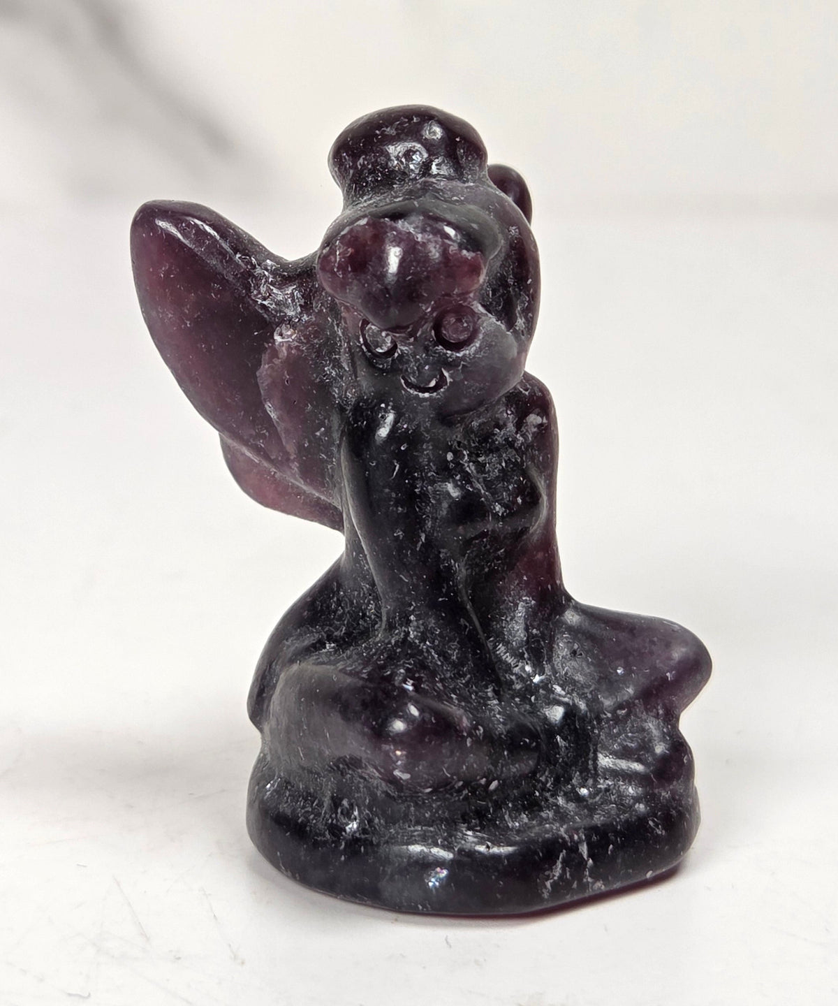 A small carved figurine of a kneeling angel or fairy made from dark polished stone, shown on a light neutral surface.