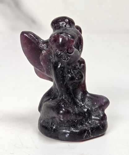 A small carved figurine of a kneeling angel or fairy made from dark polished stone, shown on a light neutral surface.