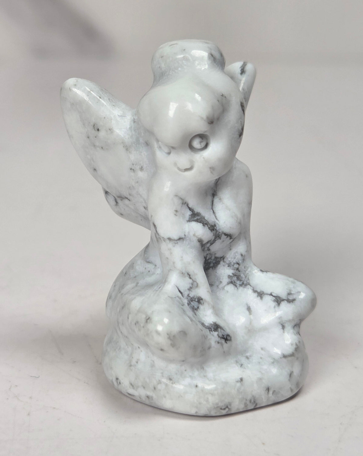 A small white marble angel figurine with gray veining, sitting on a light gray surface.
