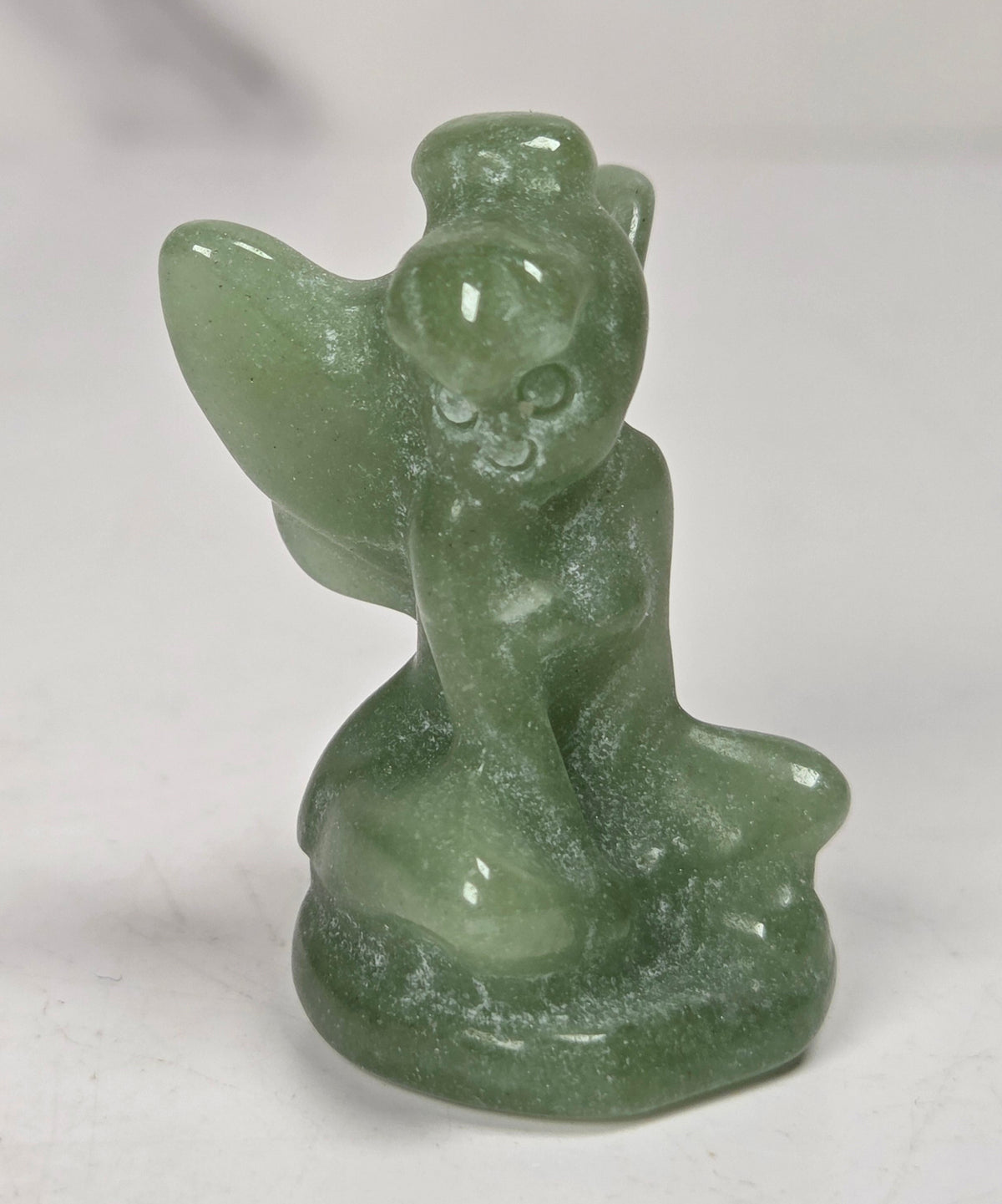 A small green crystal angel figurine with gray veining, sitting on a light gray surface.