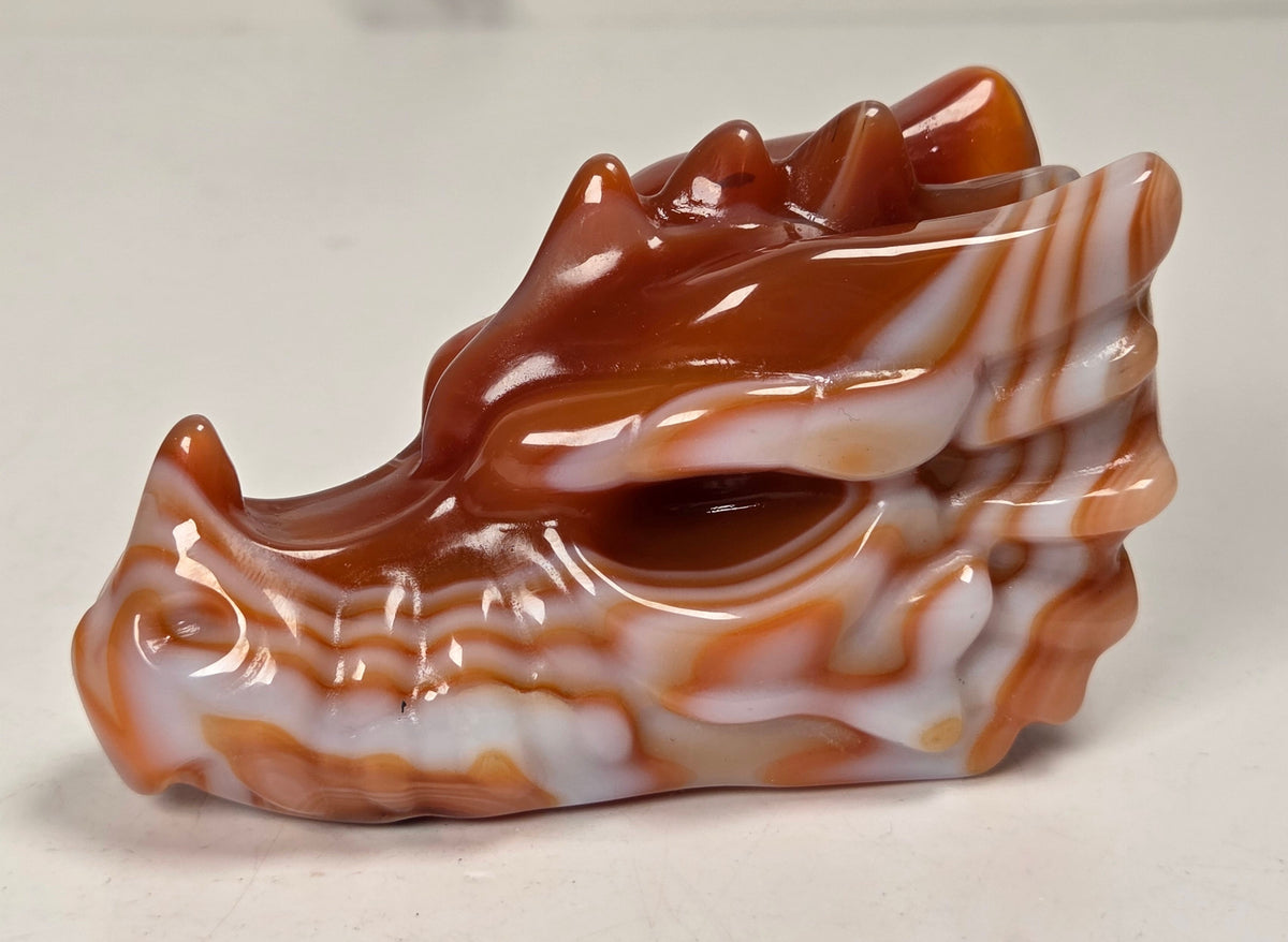 A carved orange and white marbled stone figurine, shaped like a stylized animal head with pointed ears against a plain light background.