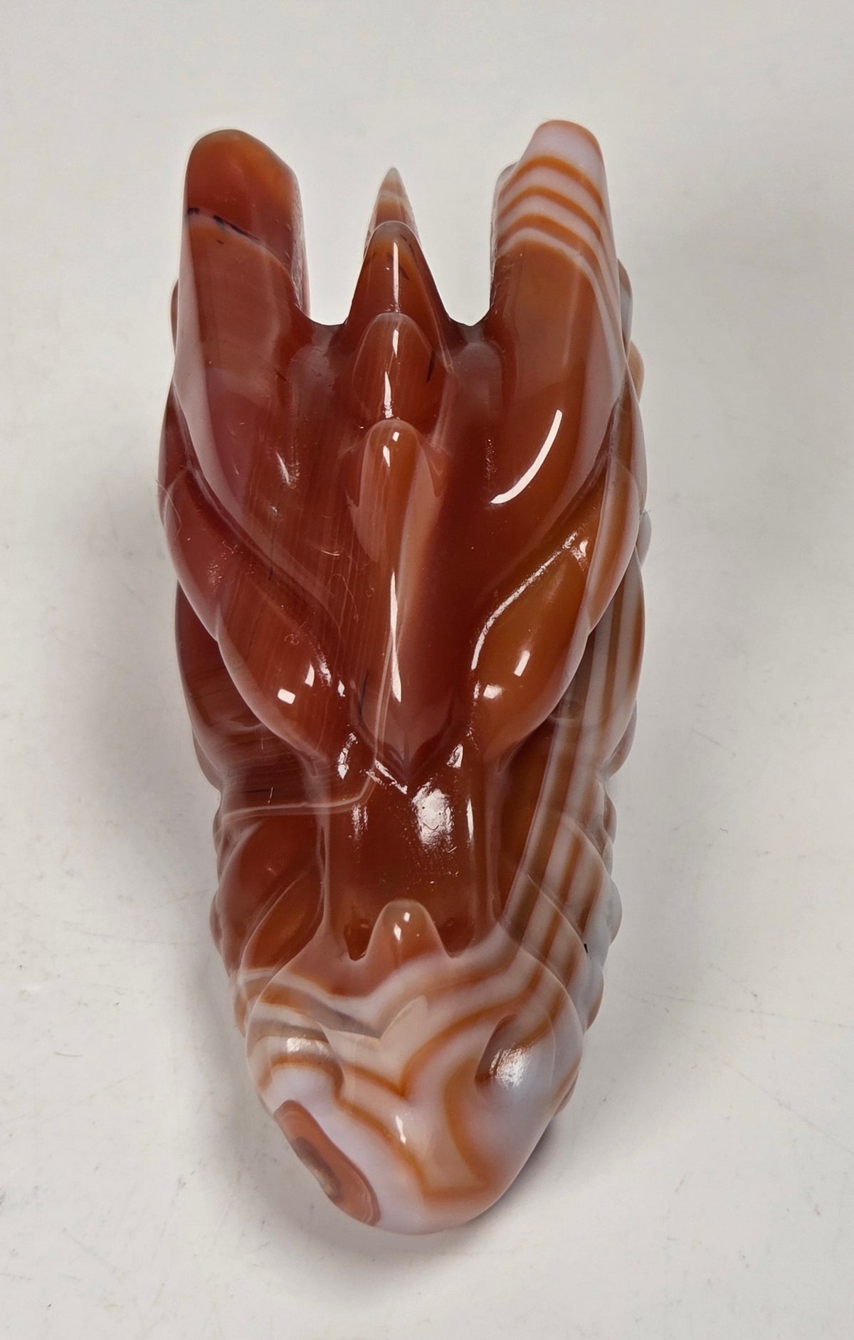 A carved orange and white marbled stone figurine, shaped like a stylized animal head with pointed ears against a plain light background.