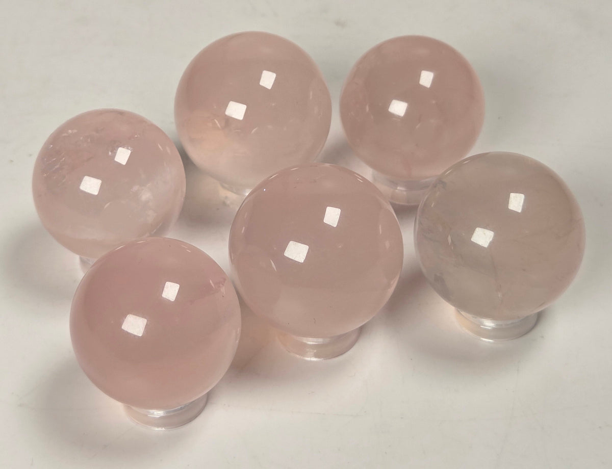 Six smooth, polished pink stone spheres arranged on a plain light background.