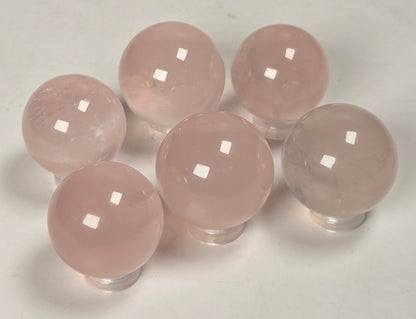 Six smooth, polished pink stone spheres arranged on a plain light background.