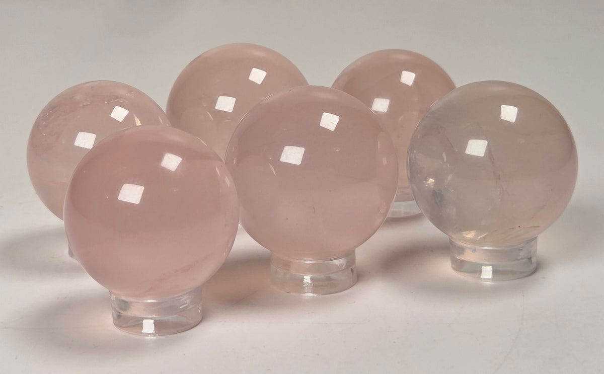 Five smooth, polished pink stone spheres displayed on clear acrylic stands against a light gray background.