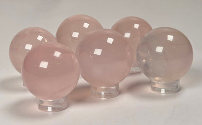Five smooth, polished pink stone spheres displayed on clear acrylic stands against a light gray background.