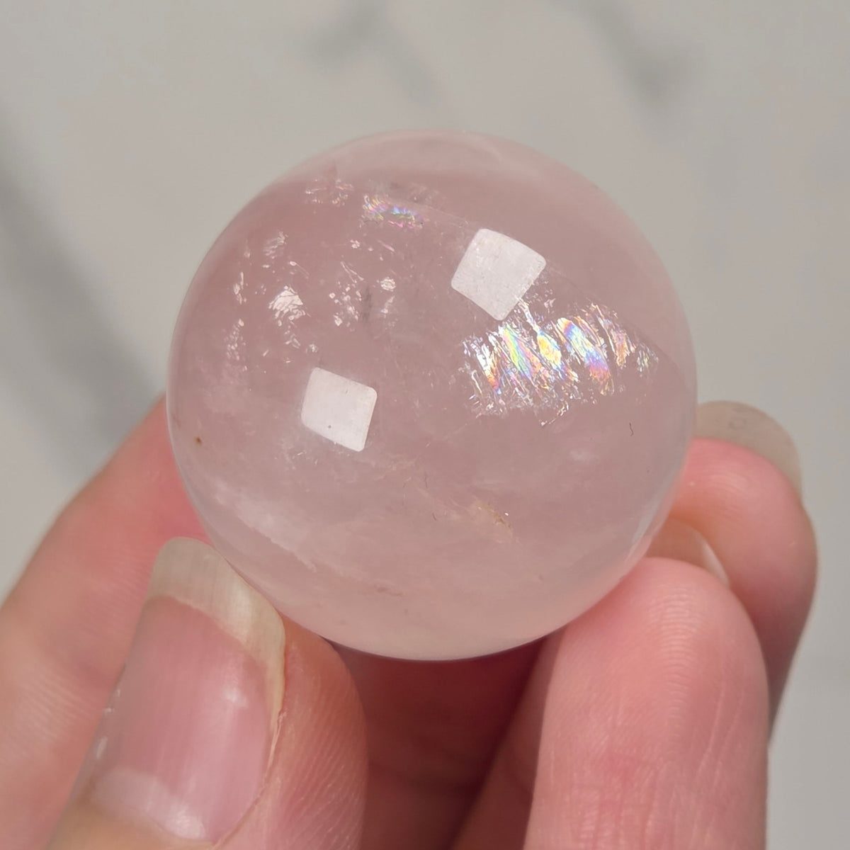 smooth, polished pink stone spheres displayed on in a hand against a light gray background.