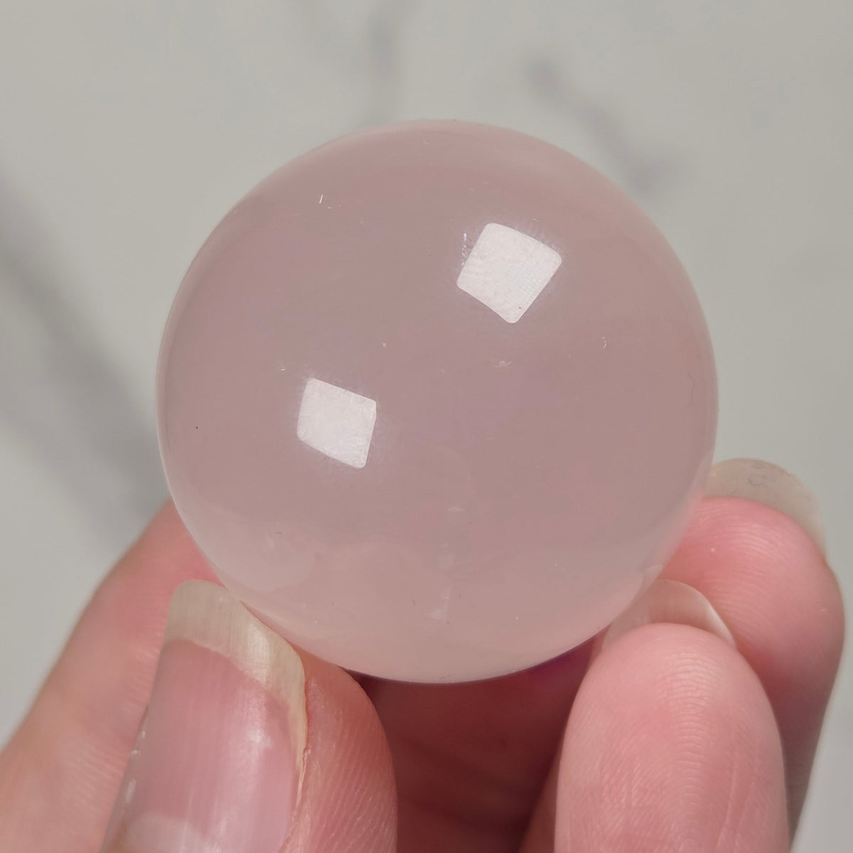 smooth, polished pink stone spheres displayed on in a hand against a light gray background.