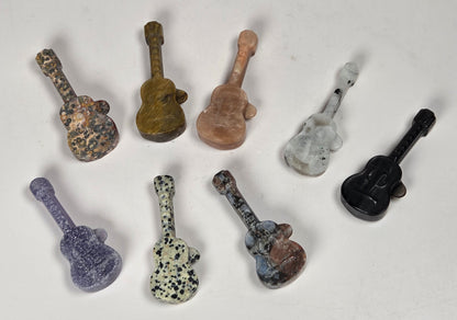 Collection of crystal guitar shaped carvings in a variety of materials and colors against a white background
