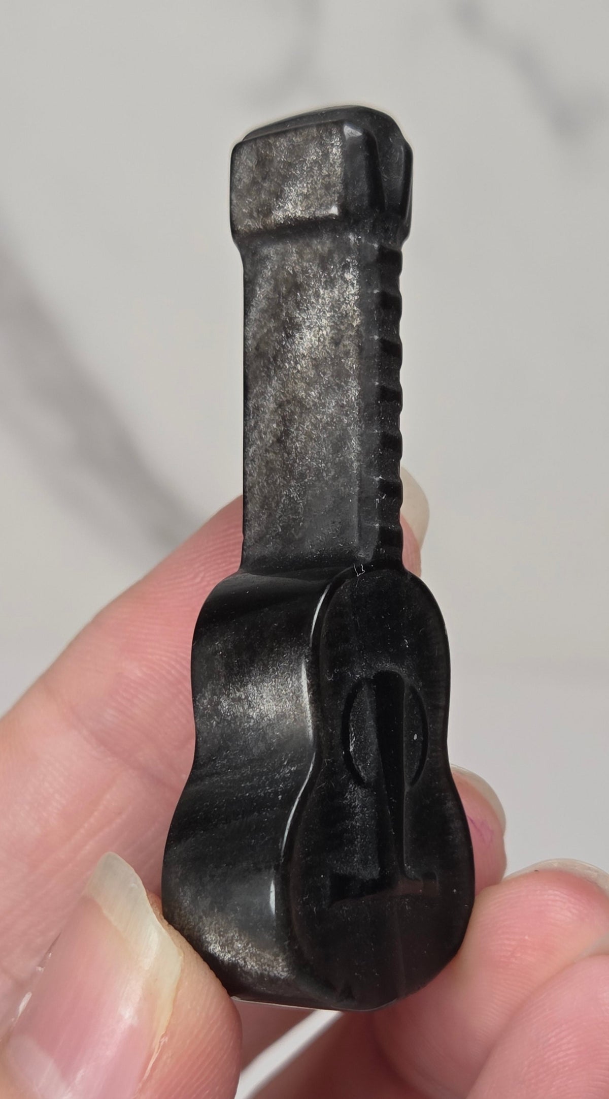 A miniature black guitar-shaped key or lock pick held between fingers against a light gray marble background.
