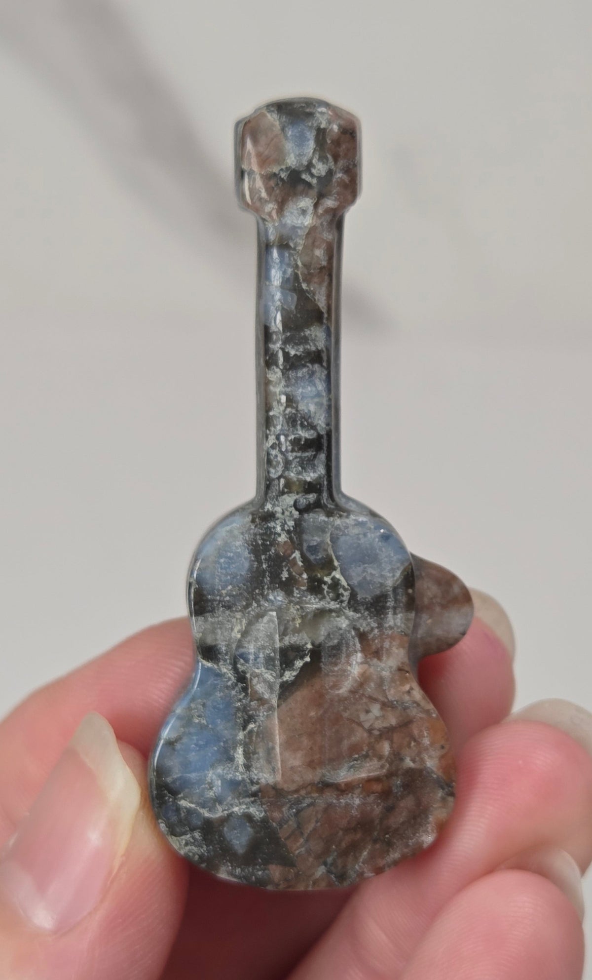 A small guitar-shaped pendant or charm made from polished stone, held between fingers against a plain light background.