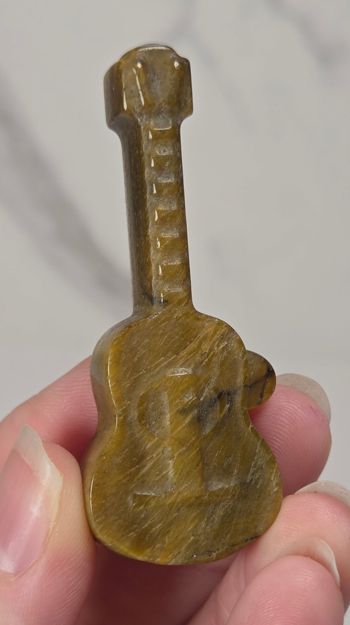 A miniature golden colored guitar-shaped stone carving held between fingers against a light gray marble background.
