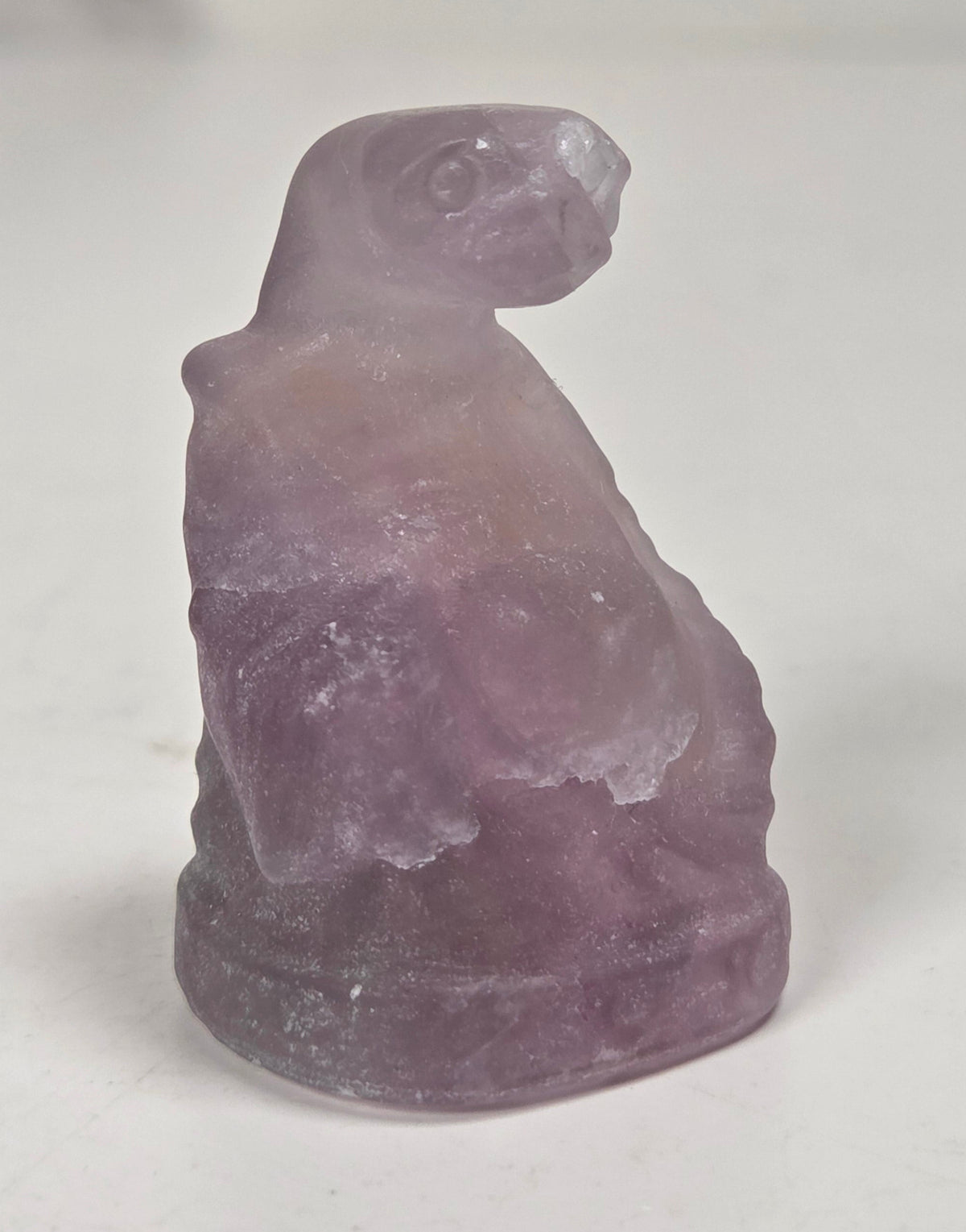 A small carved figurine of a seated figure, likely a monkey or primate, made from purple fluorite, photographed on a plain light background.