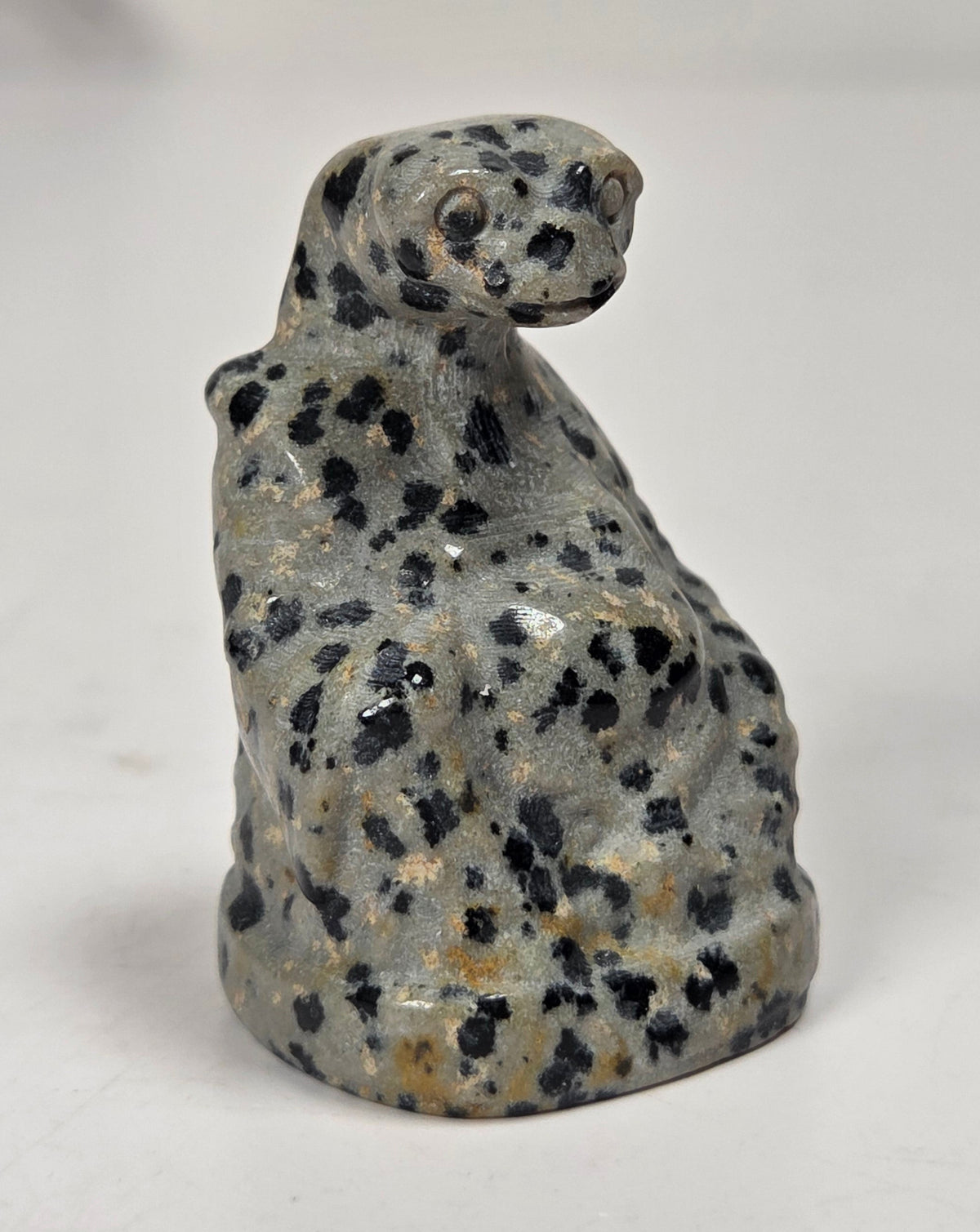A small carved figurine of a spotted cat, likely made from gray stone with black and tan speckles, standing on a light gray surface.