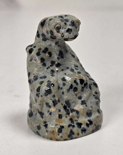 A small carved figurine of a spotted cat, likely made from gray stone with black and tan speckles, standing on a light gray surface.