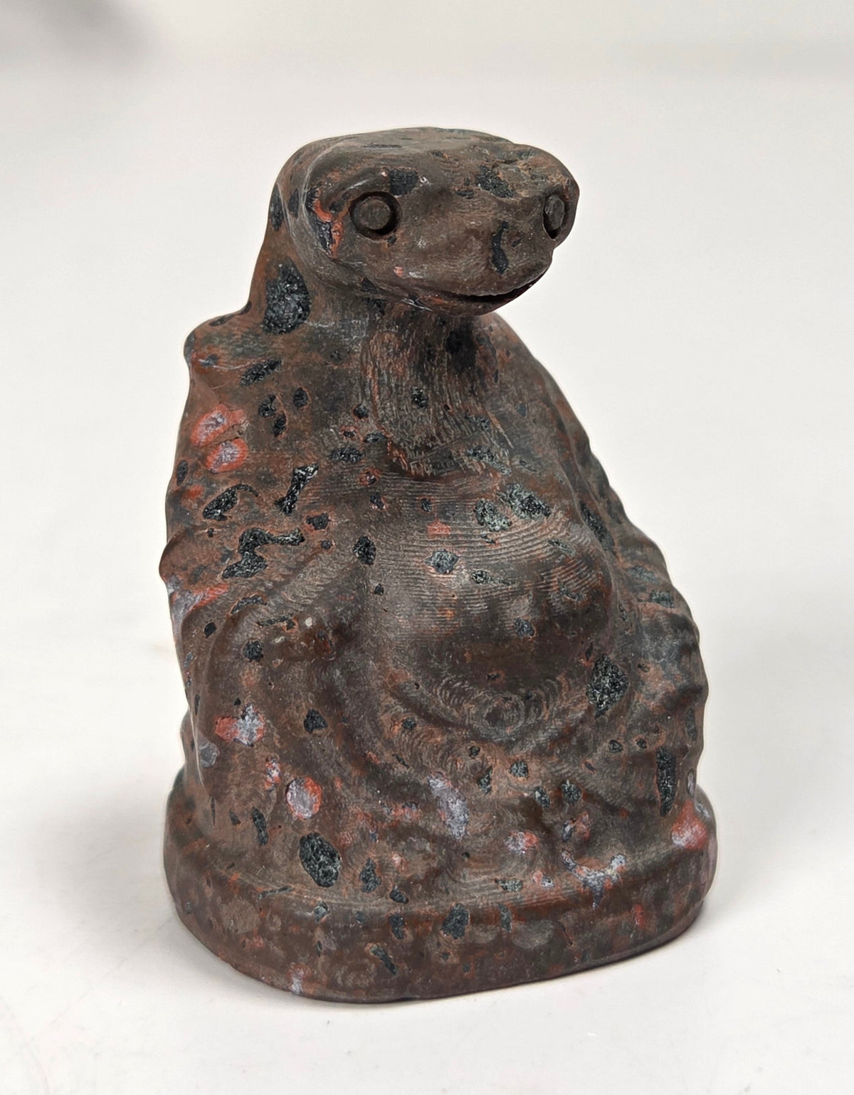 A small figurine of a seated rabbit or hare made from textured volcanic stone, featuring a dark brown and gray base with vibrant red and black mineral inclusions, set against a plain white background.