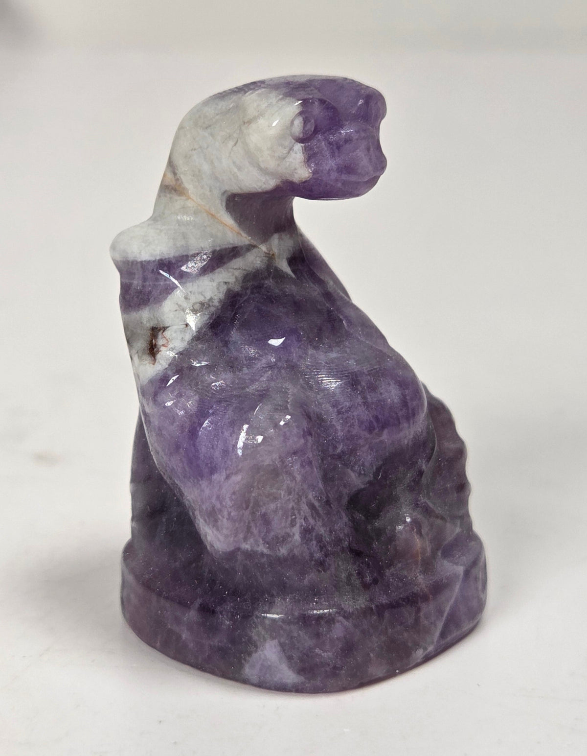 A small carved stone figurine of a seated figure with a raised head, made from purple and white marbled stone, photographed on a plain light background.