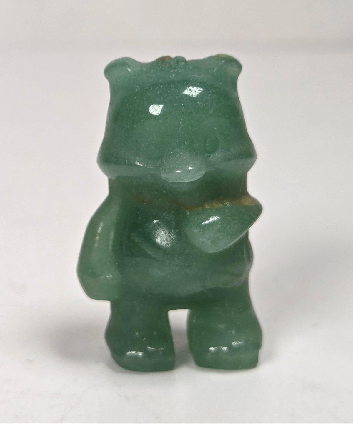 A small green translucent figurine of a bear-like character standing on a white surface against a white background.