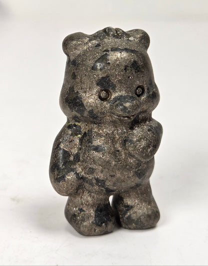 A small figurine of a bear featuring a textured gold patina with black, set against a plain light gray background.