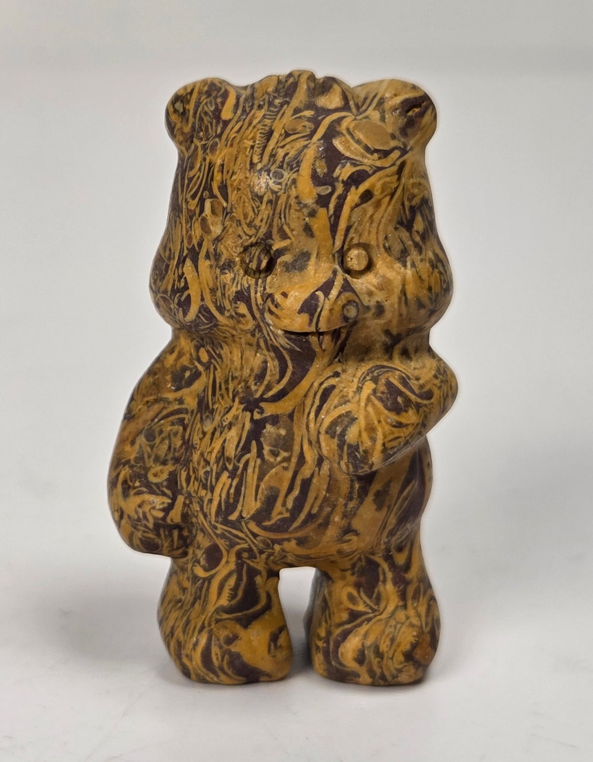 A small carved figurine of a bear with a marbled, wood-like pattern in brown and golden yellow tones, standing against a plain light background.