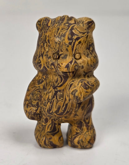 A small carved figurine of a bear with a marbled, wood-like pattern in brown and golden yellow tones, standing against a plain light background.