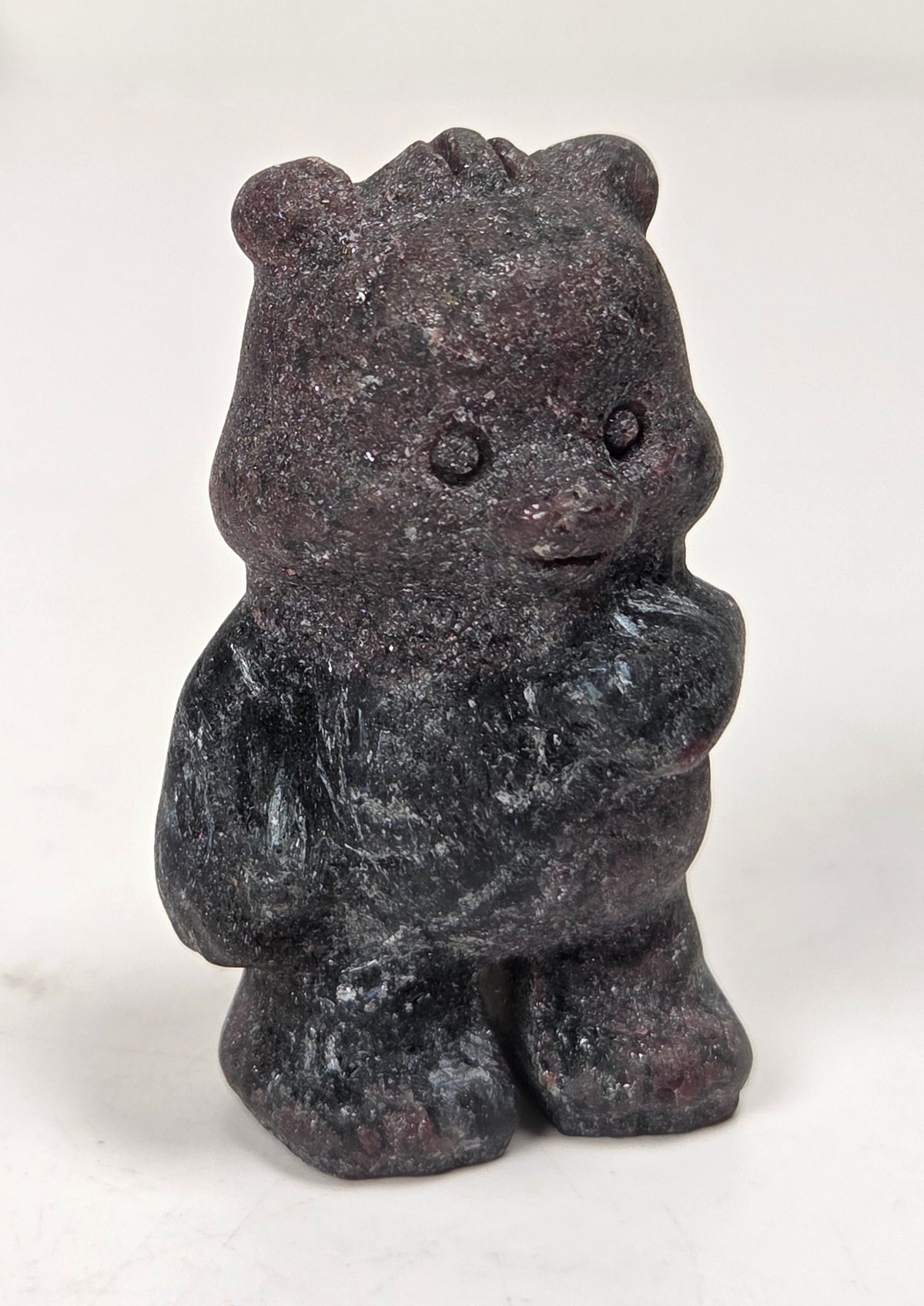 A small carved figurine of a bear made from dark volcanic stone, standing on a plain white surface.