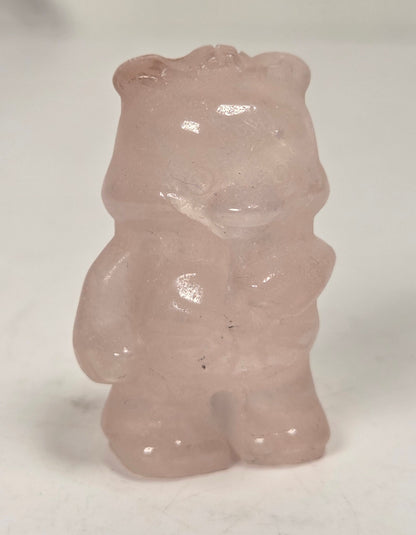 A small translucent pale pink bear figurine or gemstone standing on a plain light background.