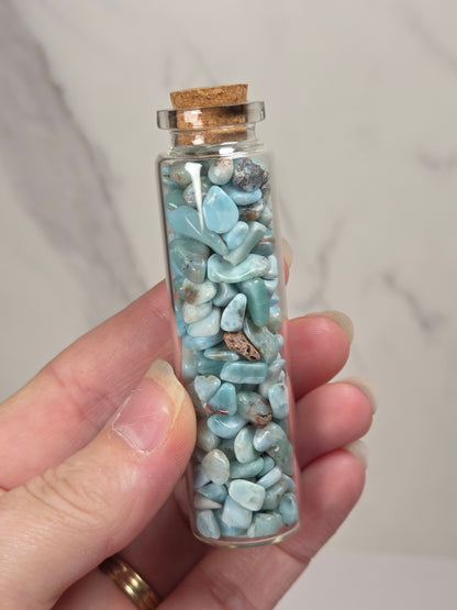 Hand holding a blue and white crystal chips in a glass bottle with a cork top against a marbled background