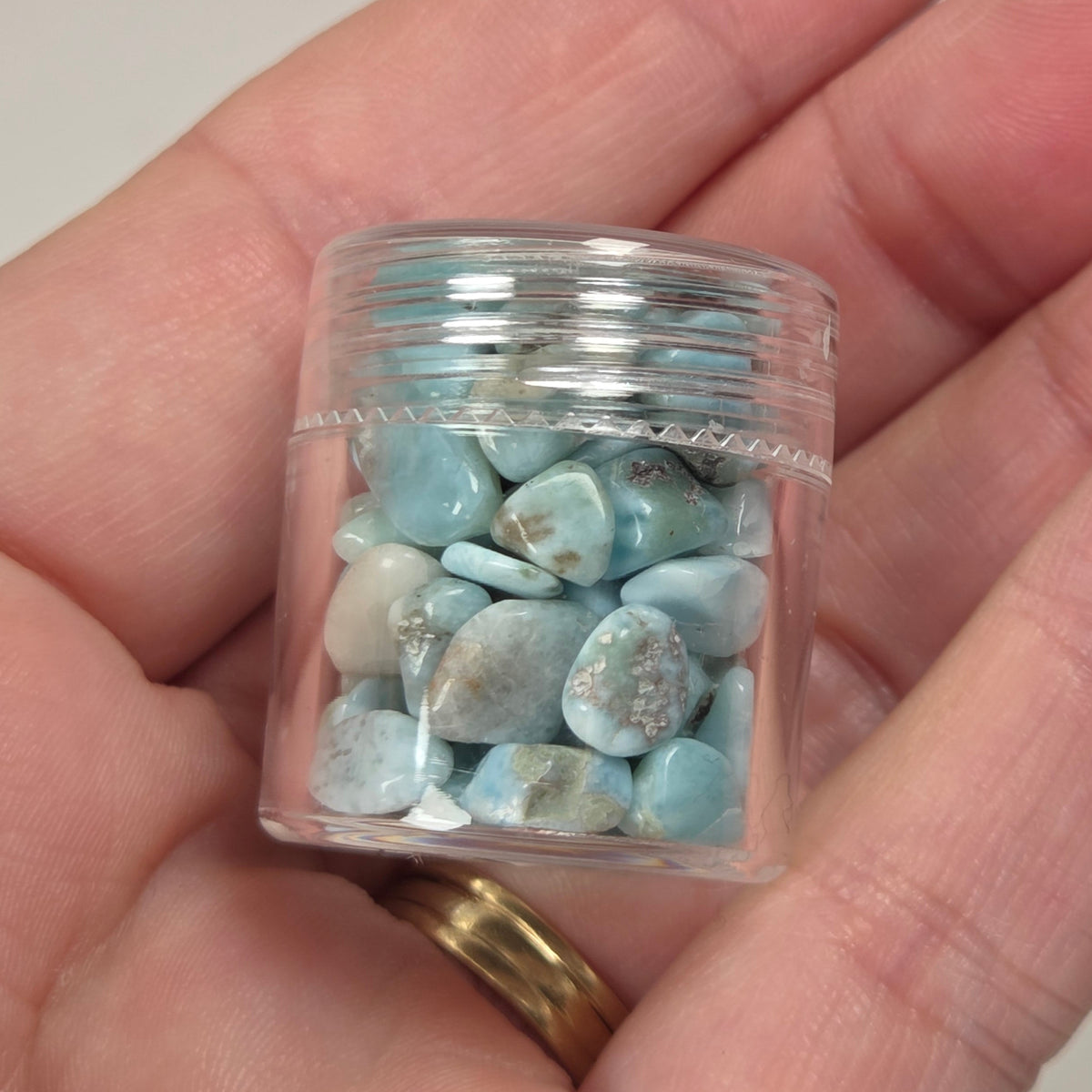 Hand holding blue and white crystal chips in a small plastic container against a marbled background