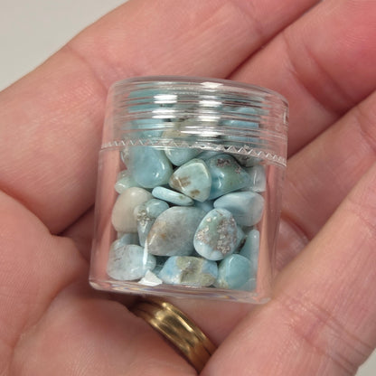 Hand holding blue and white crystal chips in a small plastic container against a marbled background