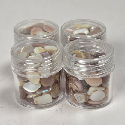 Four small clear plastic jars filled with polished stone or shell-like pieces in neutral earthy tones, arranged on a light gray surface.