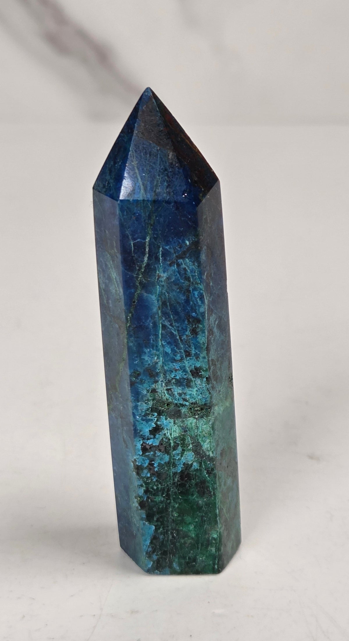 Blue-green Azurite & Chrysocolla crystal point on a white surface with a gray background