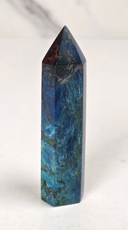 Blue-green Azurite & Chrysocolla crystal point on a white surface with a gray background