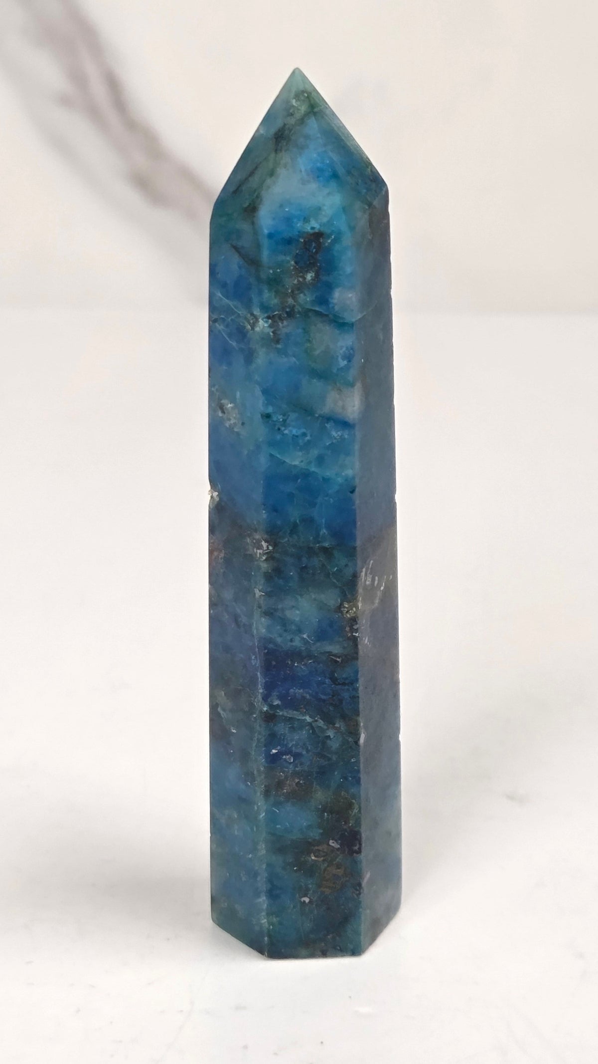 Blue-green Azurite & Chrysocolla crystal point on a white surface with a gray background