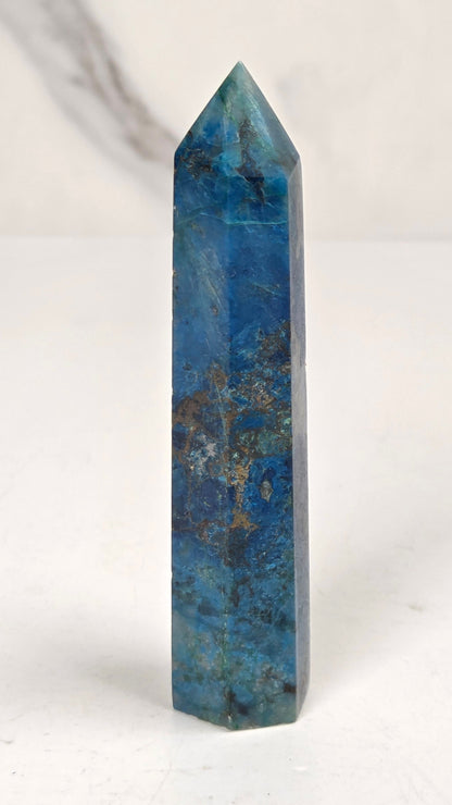 Blue-green Azurite & Chrysocolla crystal point on a white surface with a gray background