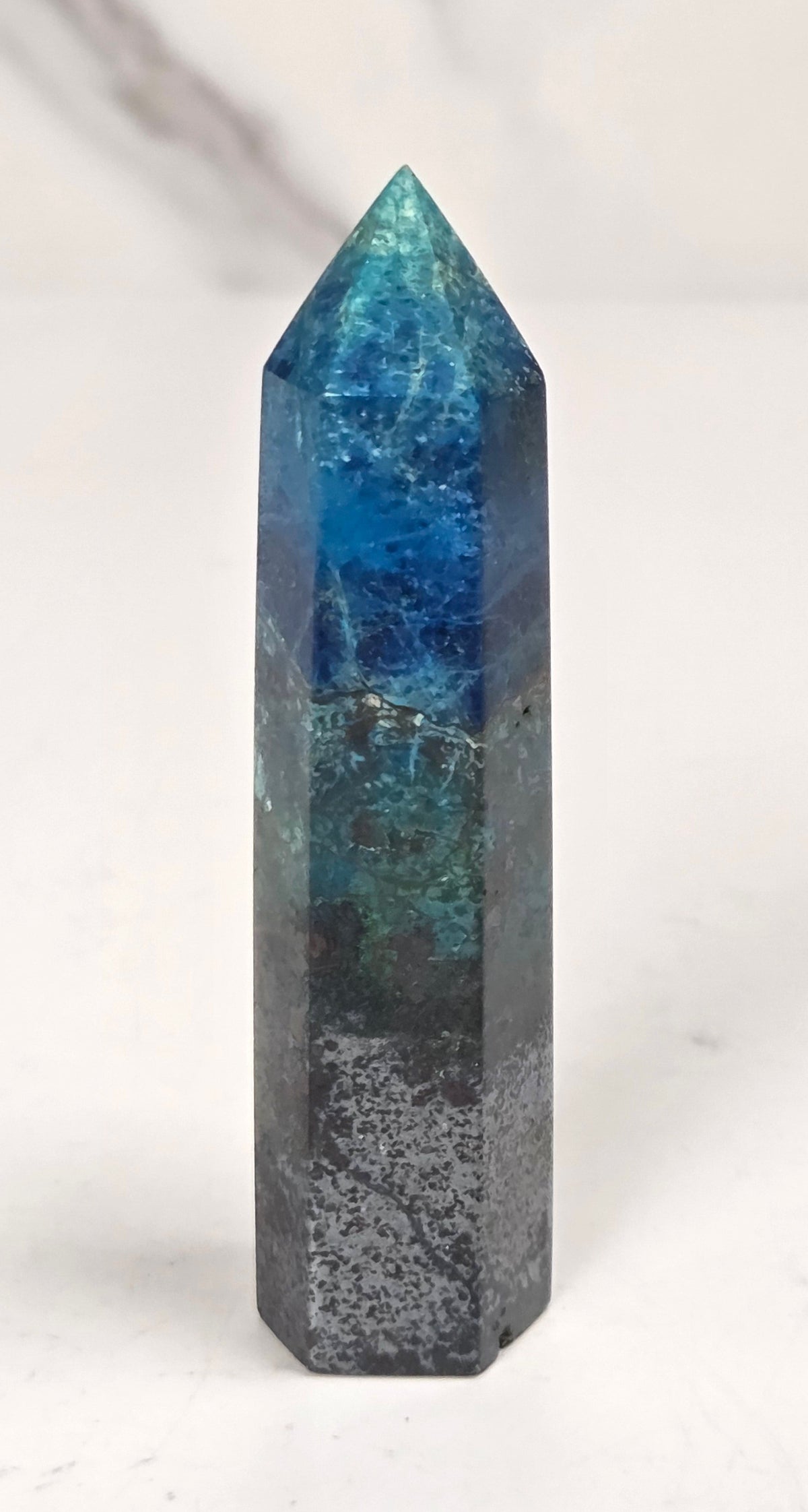 Blue-green Azurite & Chrysocolla crystal point on a white surface with a gray background