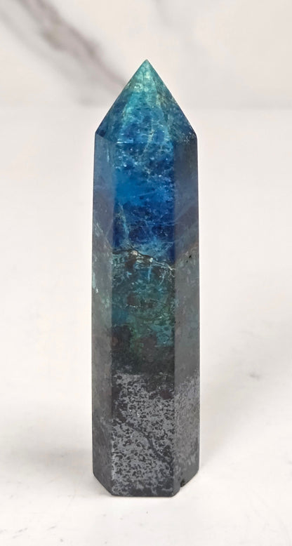 Blue-green Azurite & Chrysocolla crystal point on a white surface with a gray background