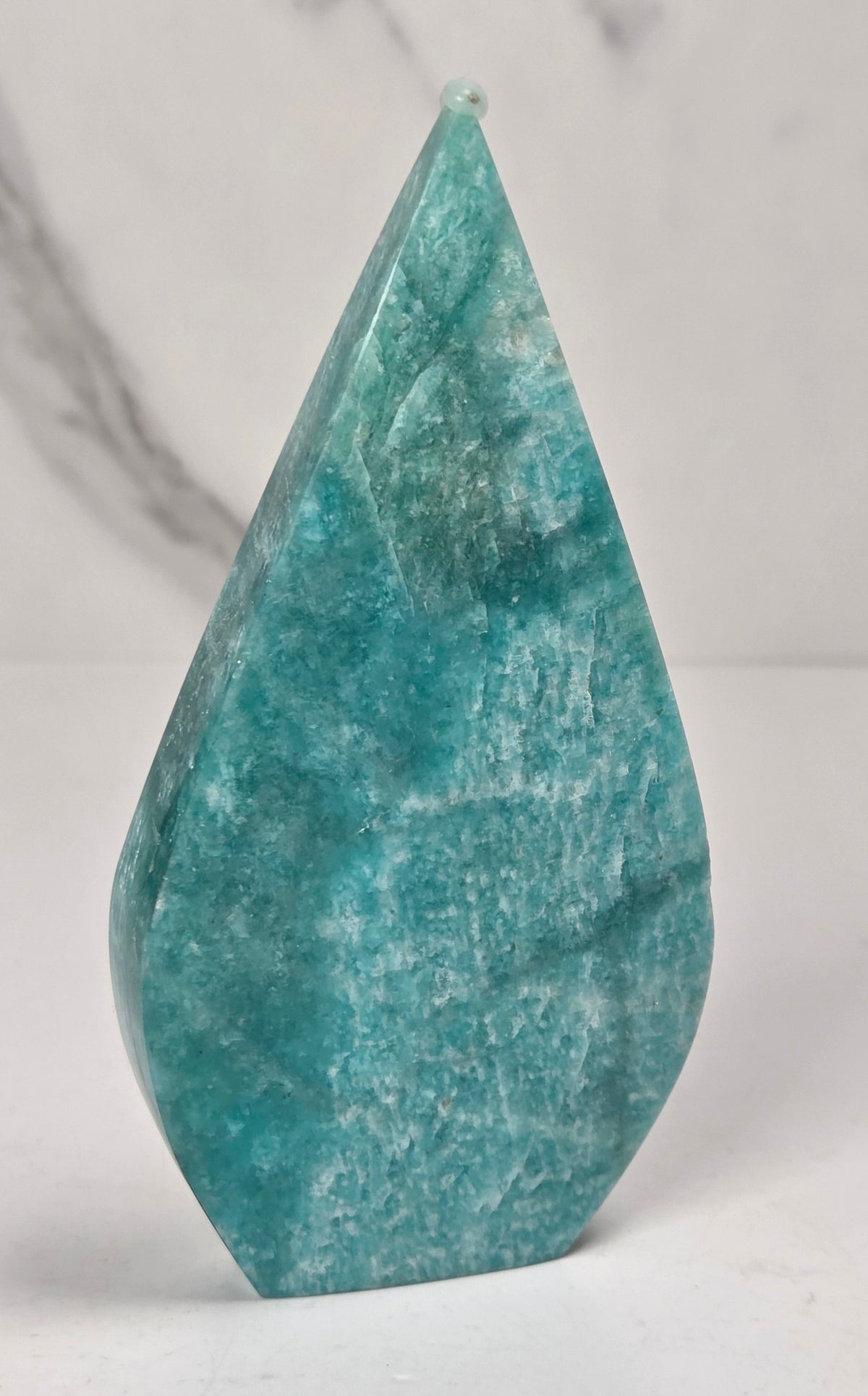 Teal green crystal carved like a teardrop on a marbled background