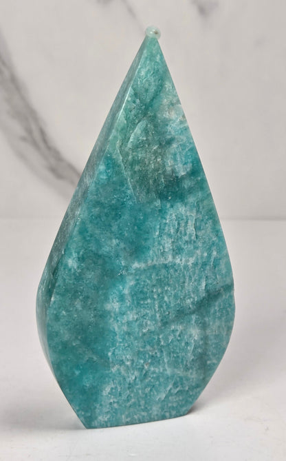 Teal green crystal carved like a teardrop on a marbled background