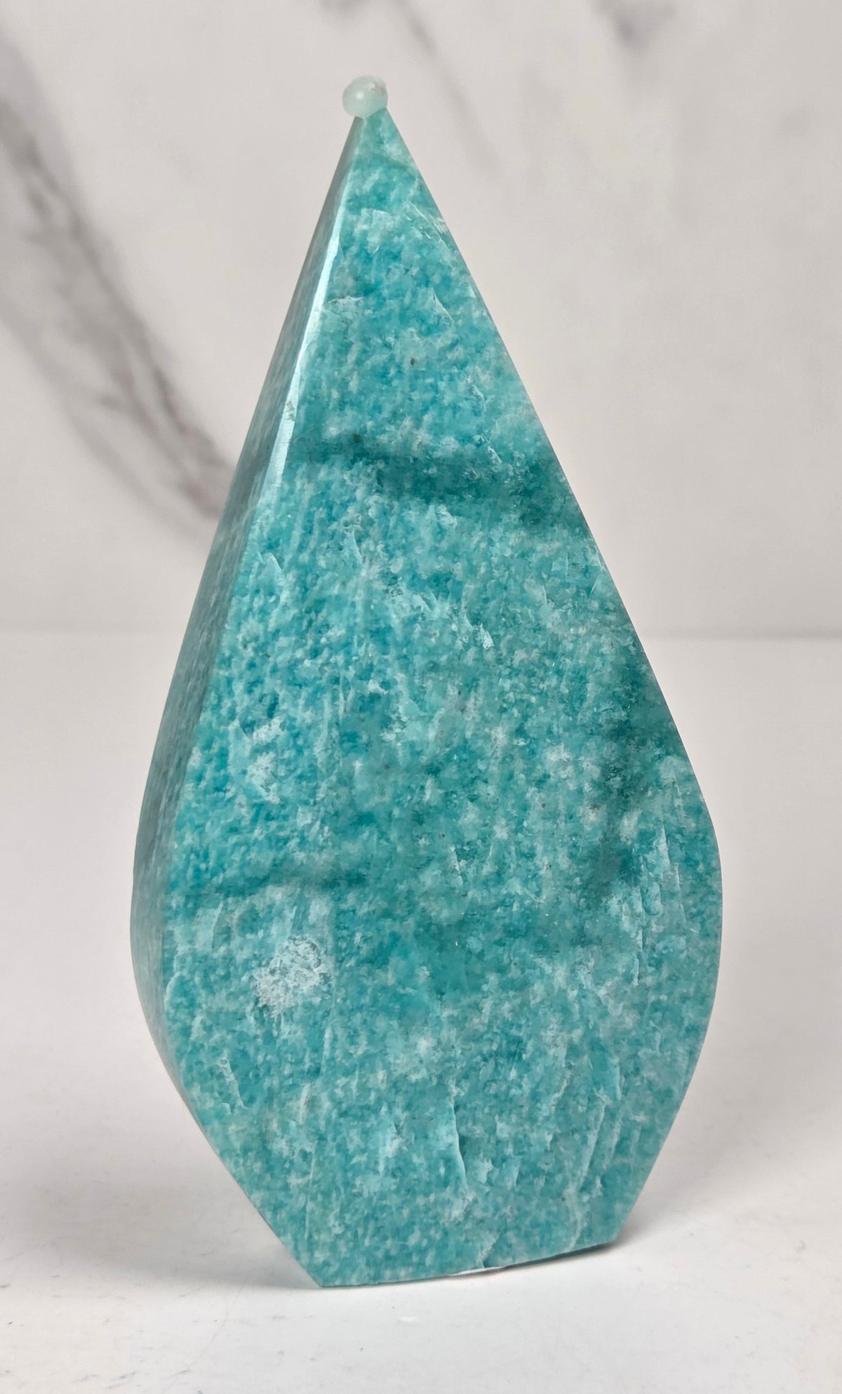Teal green crystal carved like a teardrop on a marbled background