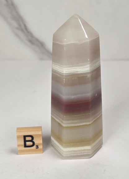 Banded calcite carved points with tan, pink, white and light green coloring against a marbled background