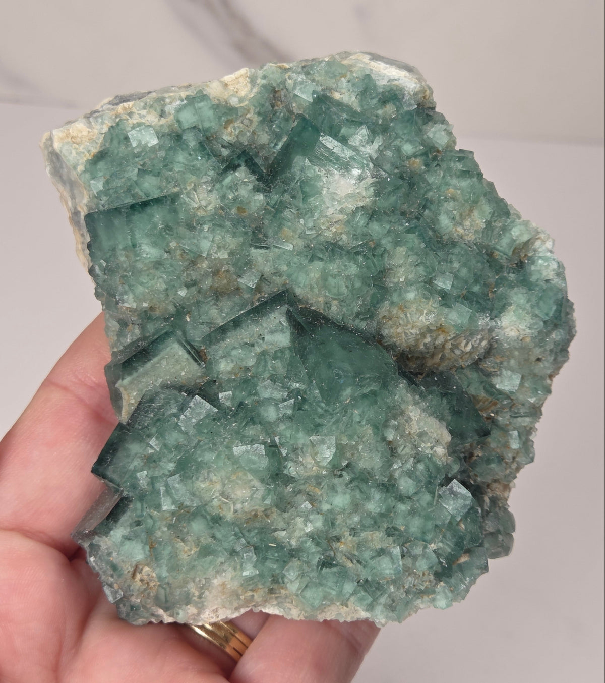 Hand holding a green fluorite specimen against a marbled grey background