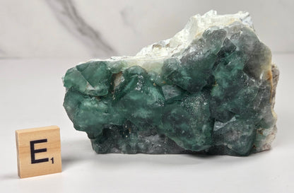 Green Fluorite specimen with a wood tile with the letter E against a marbled background