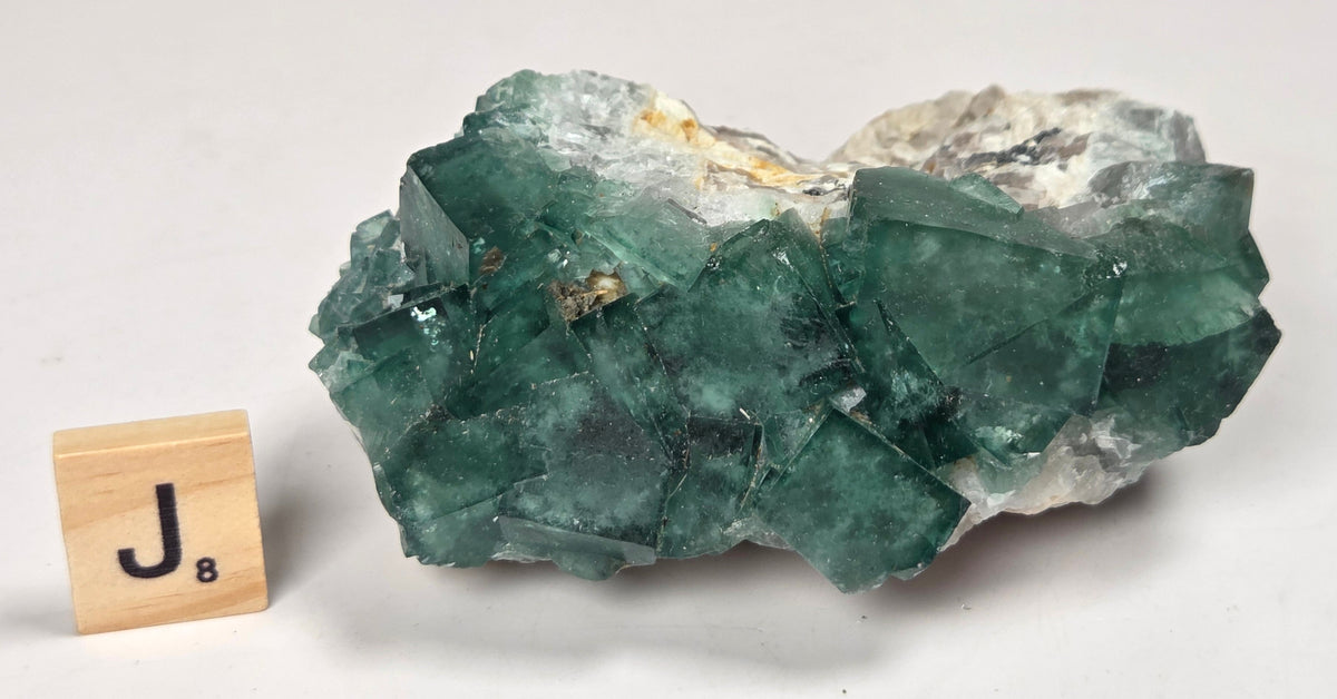 Green Fluorite specimen with a wood tile with the letter J against a marbled background