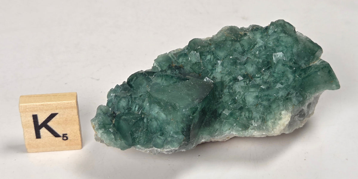 Green Fluorite specimen with a wood tile with the letter K against a marbled background