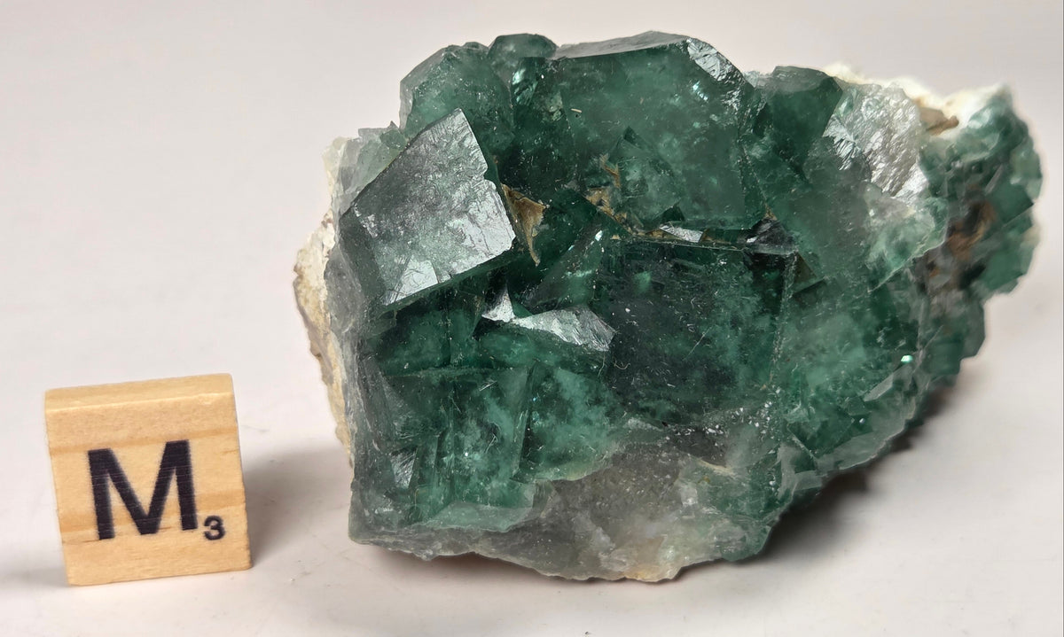Green Fluorite specimen with a wood tile with the letter M against a marbled background