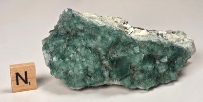 Green Fluorite specimen with a wood tile with the letter A against a marbled background