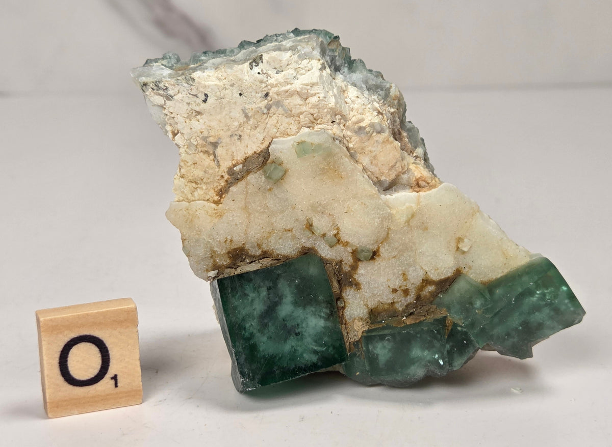 Green Fluorite specimen with a wood tile with the letter A against a marbled background