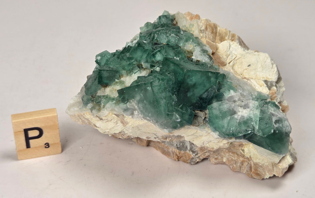 Green Fluorite specimen with a wood tile with the letter P against a marbled background